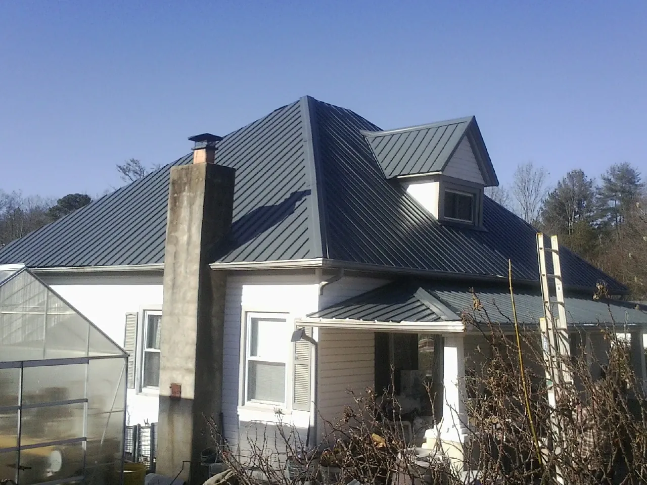 Dark blue standing seam metal roof on a white farmhouse with dormer — Slate & Tile Roof Repair by Roofing Brothers in Lindon