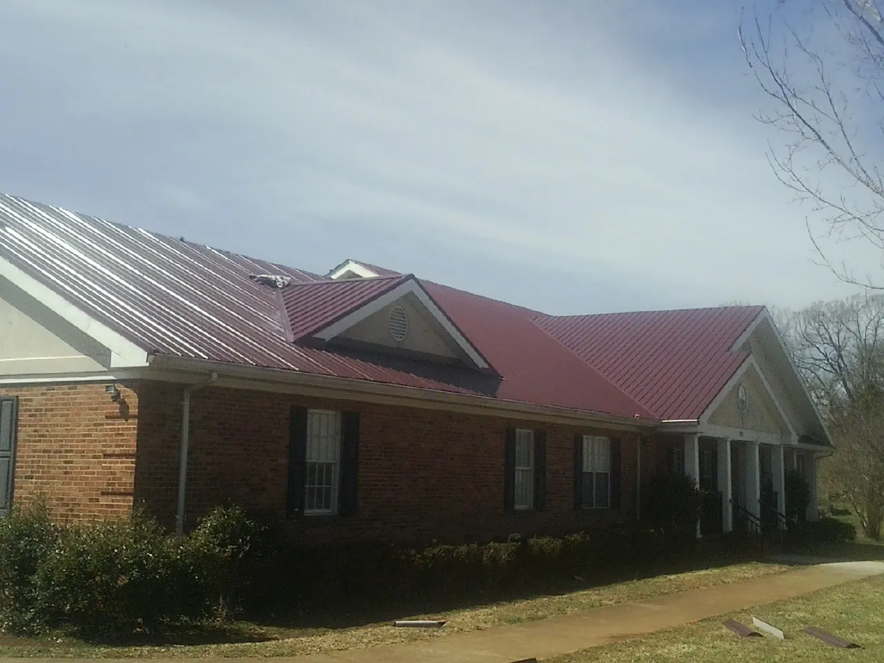 Red metal roof with gabled entries on a long brick building, from a Hail Damage Roof Repair job in Lindon
