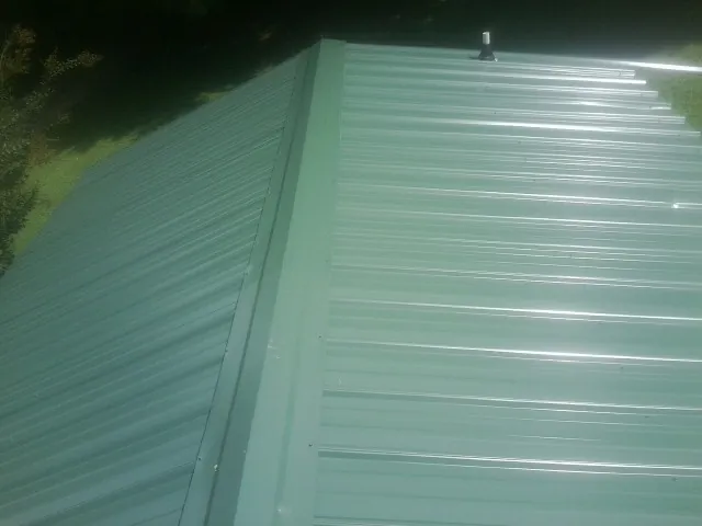 New green metal panels meeting at the ridge of a roof — Flat Roof Repair work by our crew in Lindon